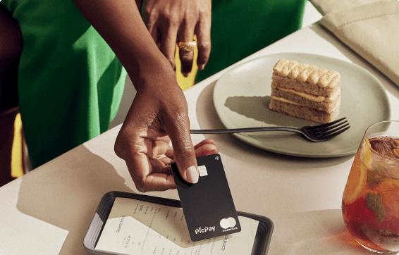 Mulher segurando um cartão de crédito picpay black e aproximando no celular