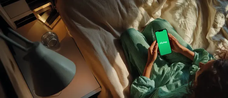 Pessoa em ambiente externo, segurando um smartphone na altura do rosto com a tela mostrando o logo do PicPay..